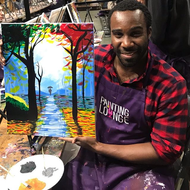 Tramell Tillman in a red-lack check shirt and painting apron holding his first beautiful painting.